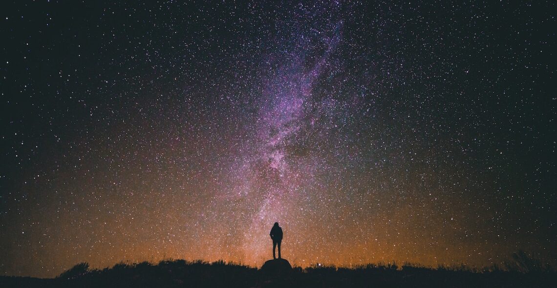 Person standing on a rock looking up at stars in the sky