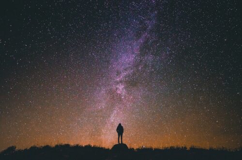 Person standing on a rock looking up at stars in the sky